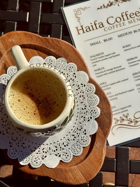 A cup of coffee beside a Haifa Coffeehouse menu in direct sunlight
