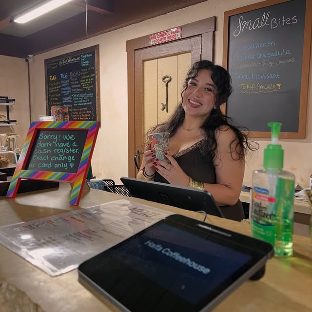 The Haifa Coffeehouse counter with handwritten boards and a smiling person holding a patterned cup